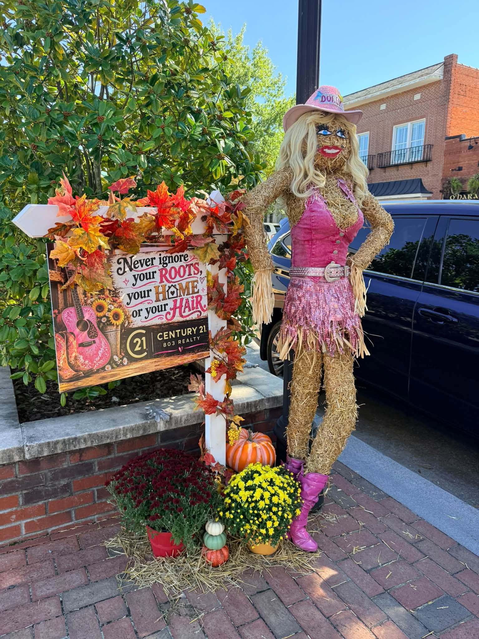 Pink cowgirl scarecrow beside a Century 21 sign on Main Street during the Lexington Scarecrow Stroll